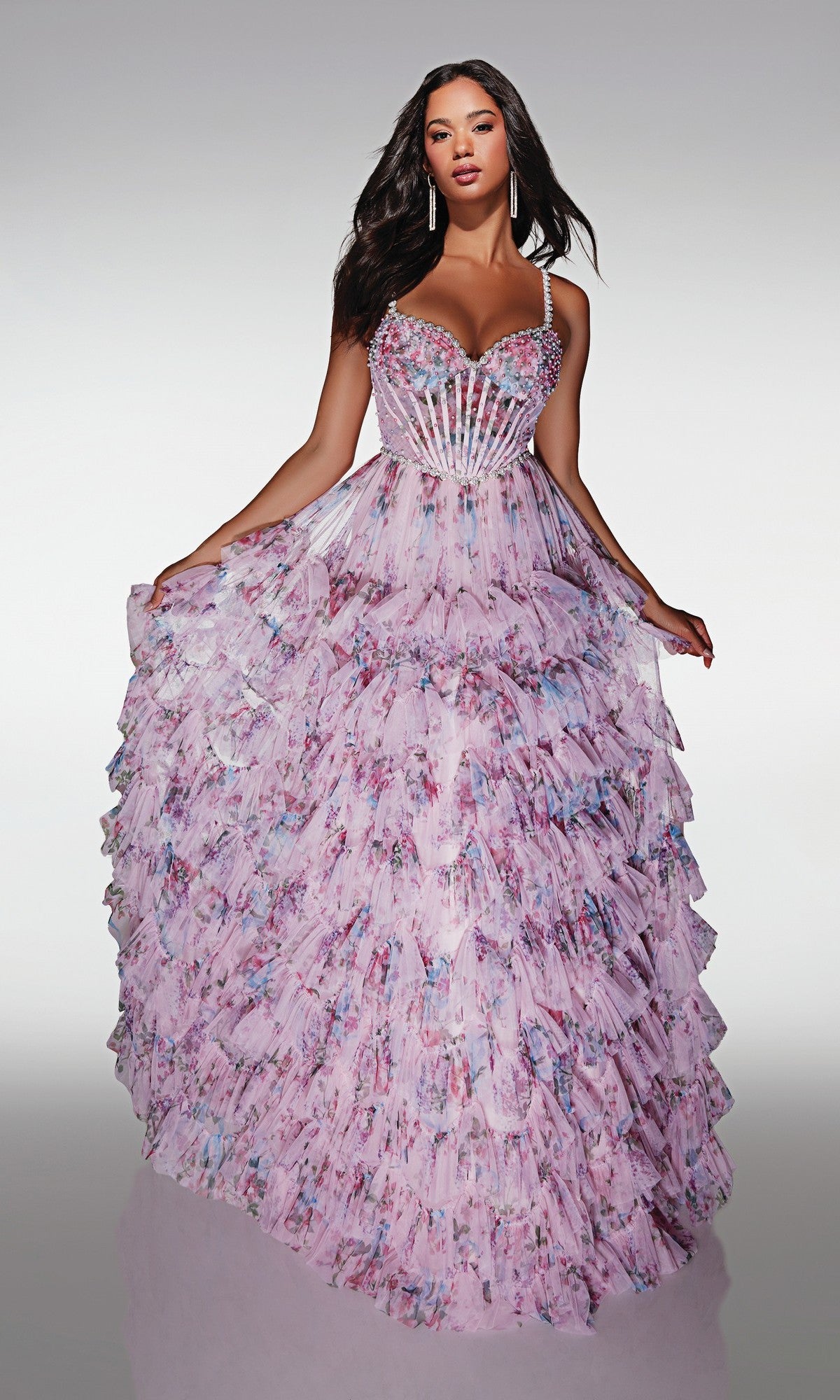 A woman models the Alyce 62182 long prom dress—a light purple floral ball gown with a sheer corset bodice, thin straps, beaded accents, and a layered skirt—posing against a plain light background.